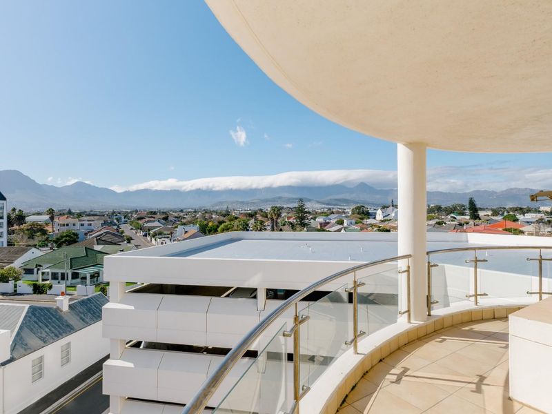 Spacious curved balcony featuring a modern glass balustrade and tiled flooring, offering expansive panoramic views of the surrounding neighborhood and distant mountains.