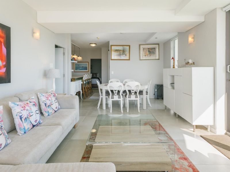 Bright open-plan living and dining area featuring neutral tiled flooring, recessed lighting, and large sliding glass doors leading to an outdoor space.