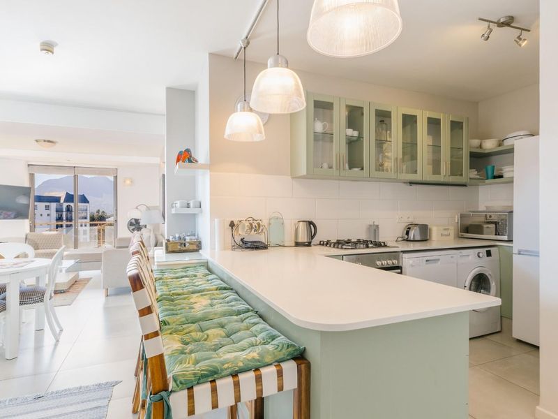 Bright open-plan kitchen and living area featuring a breakfast bar, modern cabinetry, gas hob, and tiled flooring, flowing into a spacious dining and lounge area.