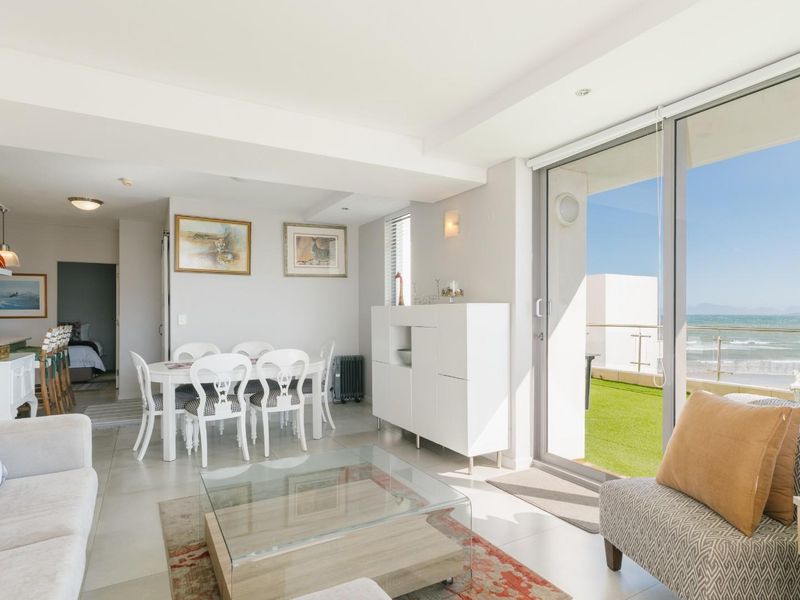 Bright open-plan living and dining area featuring large sliding glass doors that open onto a balcony with ocean views.