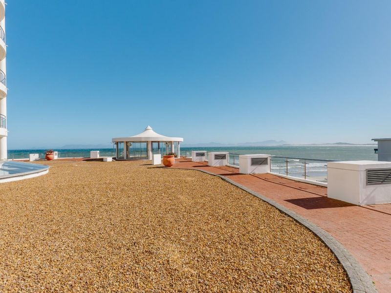 Expansive rooftop terrace featuring a paved walkway, gravel landscaping, a central gazebo, and glass balustrades with panoramic ocean views.