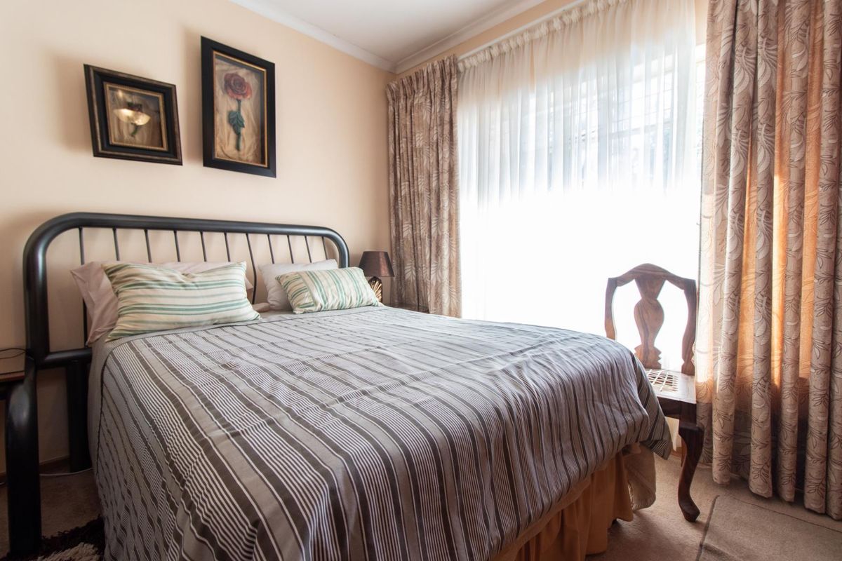A cozy bedroom featuring neutral wall tones, carpeted flooring, and large windows dressed with floor-to-ceiling curtains, providing ample natural light.