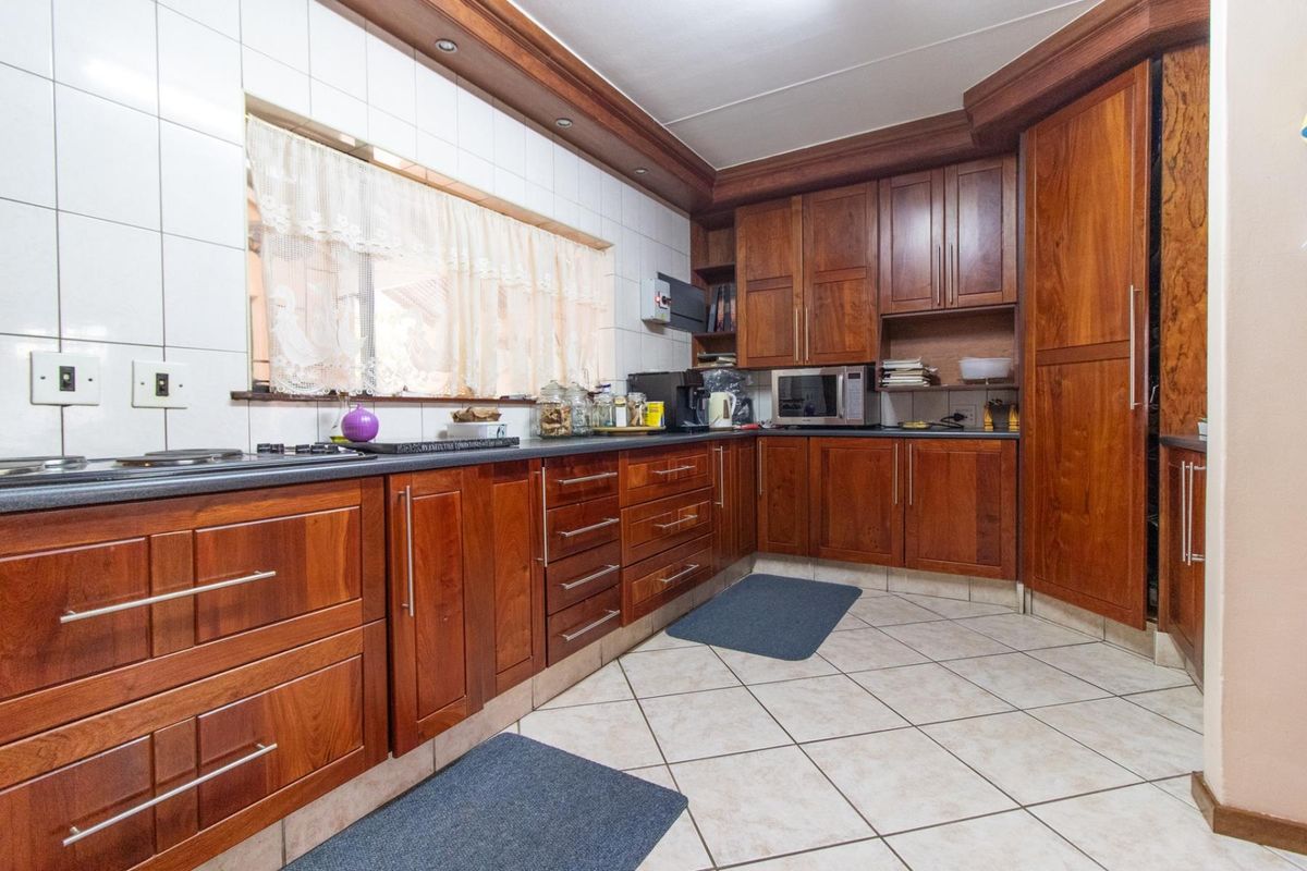 A functional kitchen featuring warm-toned wooden cabinetry, tiled splashbacks, and tiled flooring, offering ample storage and workspace for daily meal preparation.