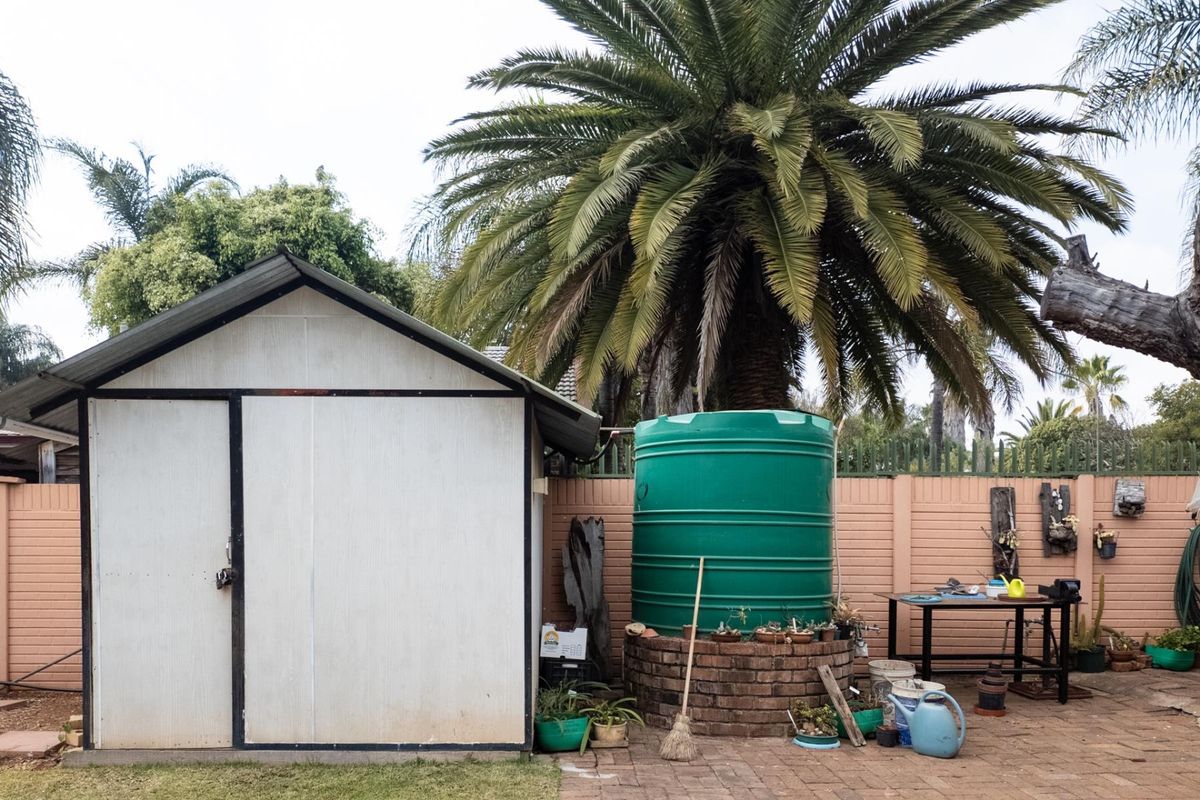 Rear garden area featuring a storage shed, a large green water tank on a brick base, and paved patio space.