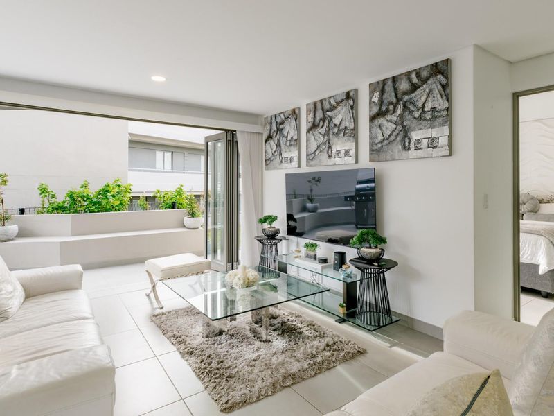 Bright and modern living room featuring large bi-fold glass doors that open onto a private balcony, with neutral tiled flooring and recessed lighting.