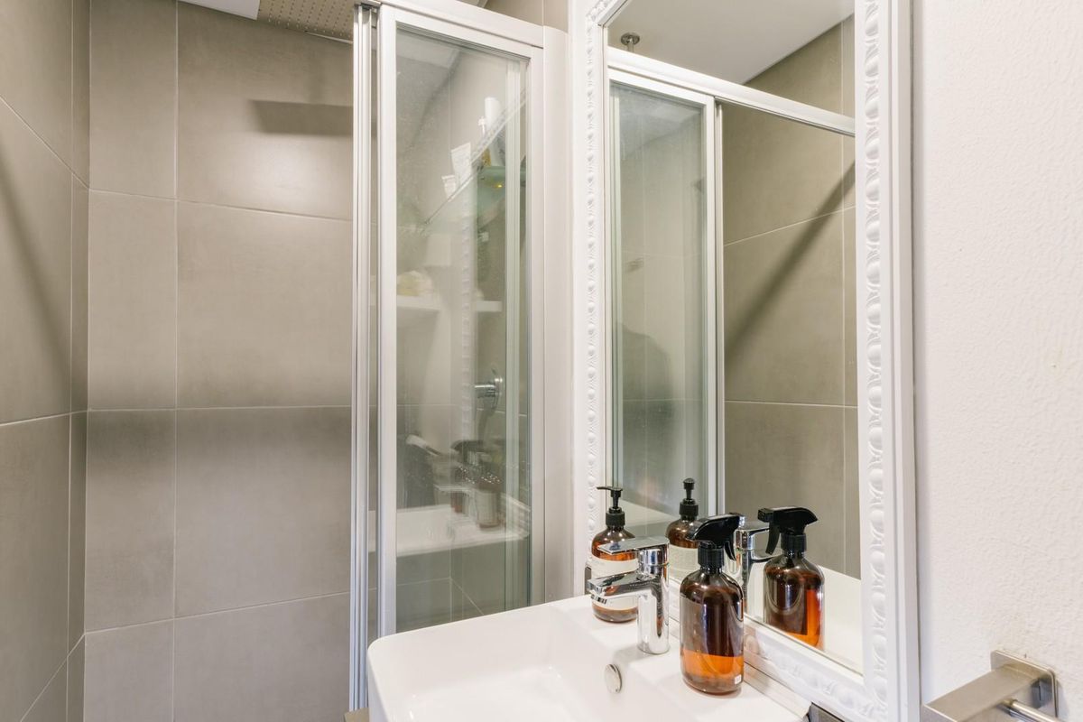 A modern bathroom featuring a tiled shower enclosure, a vanity basin with a mixer tap, and a decorative framed mirror.