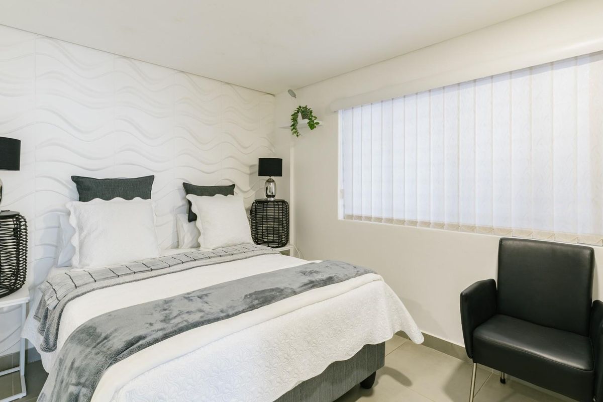 A well-maintained bedroom featuring a modern textured feature wall, neutral tiled flooring, and vertical window blinds for privacy.