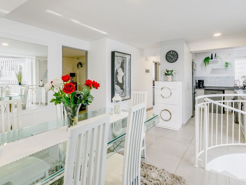 Bright open-plan living and dining area featuring tiled floors, modern kitchen with subway tile backsplash, and a distinctive spiral staircase railing.