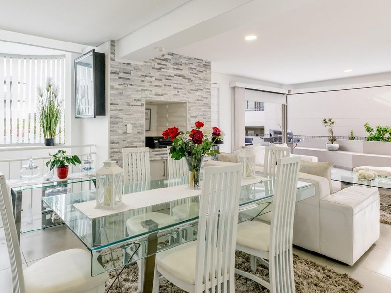 Bright open-plan living and dining area featuring a stone-clad feature wall with a built-in braai, tiled floors, and seamless access to the outdoor patio.