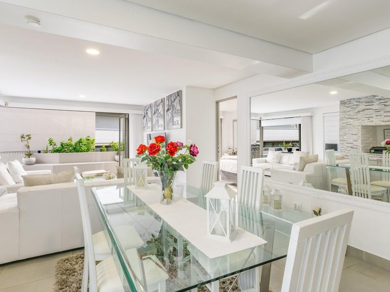 Bright and spacious open-plan living and dining area featuring a stone accent wall, large wall mirror, and seamless flow to the outdoor patio.