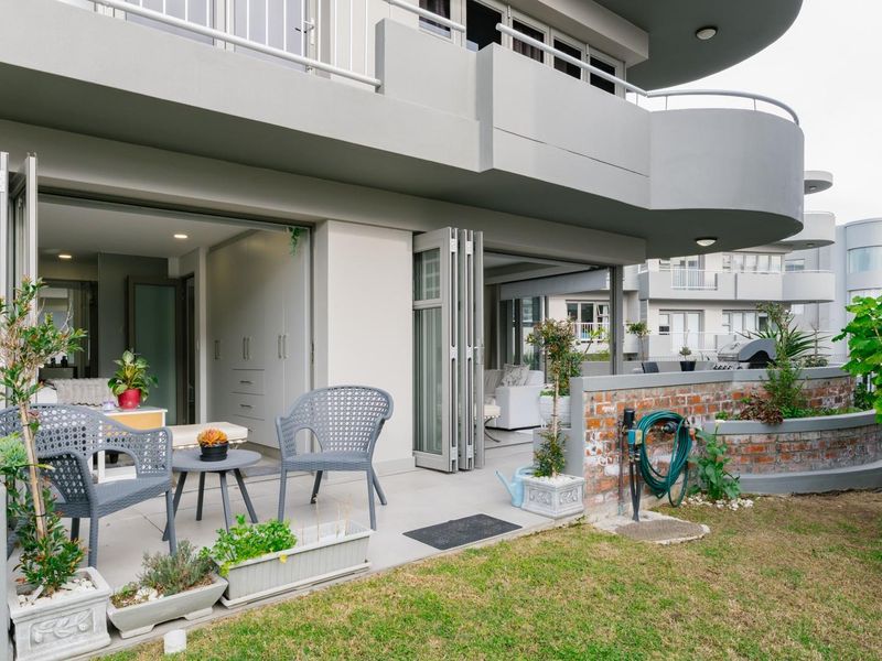 A spacious ground-floor patio featuring tiled flooring, bi-fold doors leading to the interior, and a charming brick planter wall overlooking the garden area.