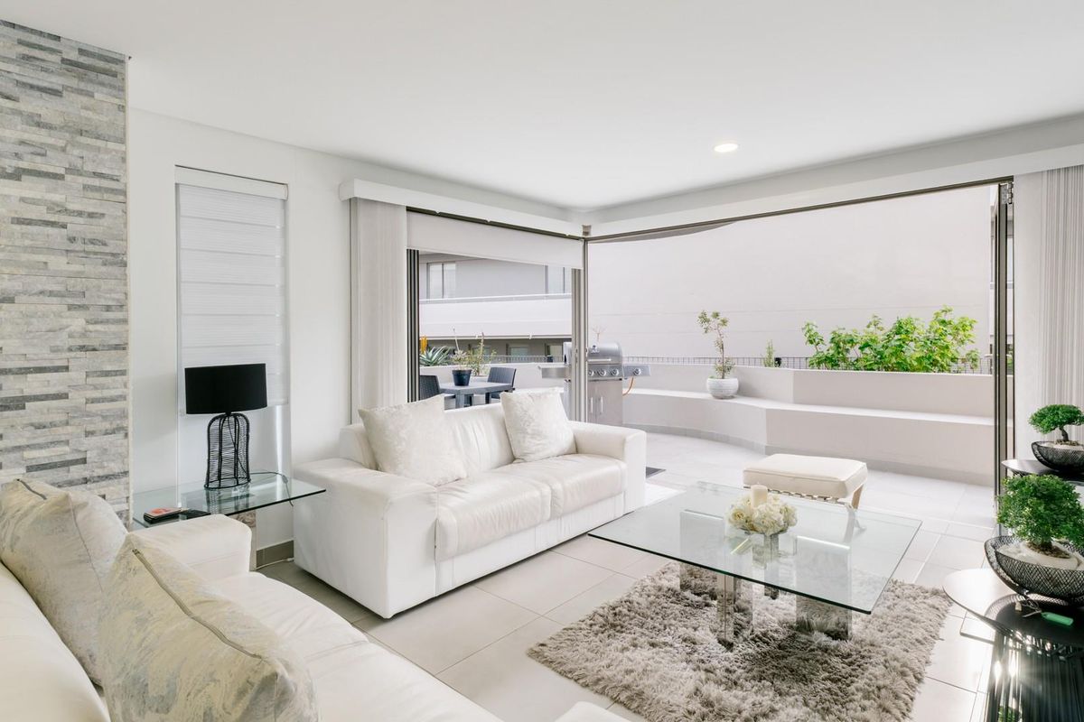 Bright open-plan living area featuring a stacked stone accent wall, tiled floors, and seamless transition to a spacious balcony through large sliding glass doors.