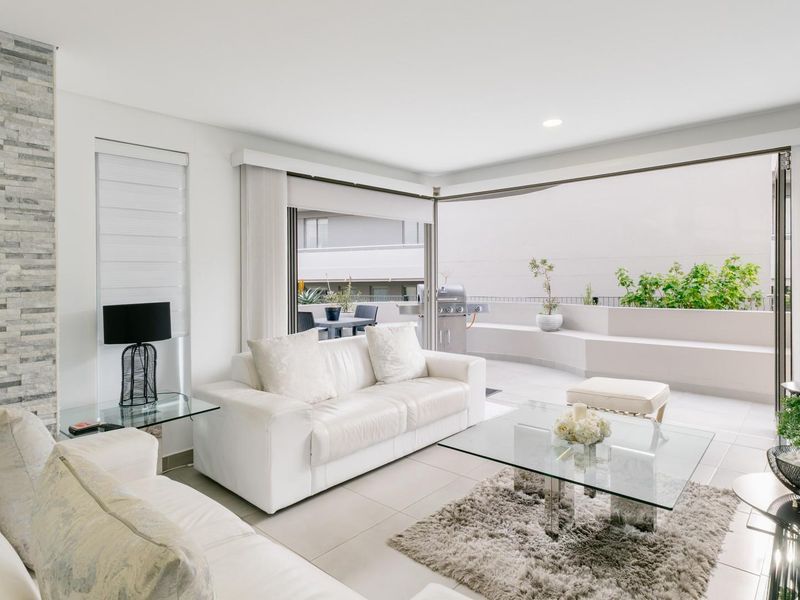 Bright open-plan living area featuring a stacked stone accent wall, tiled floors, and seamless transition to a spacious balcony through large sliding glass doors.