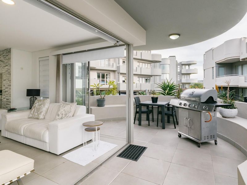 Spacious open-plan living area featuring seamless indoor-outdoor flow to a large curved balcony with tiled flooring and modern finishes.
