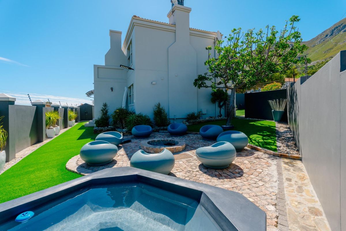 A well-maintained rear garden featuring a built-in fire pit area, cobblestone paving, artificial lawn, and a plunge pool set against a mountain backdrop.
