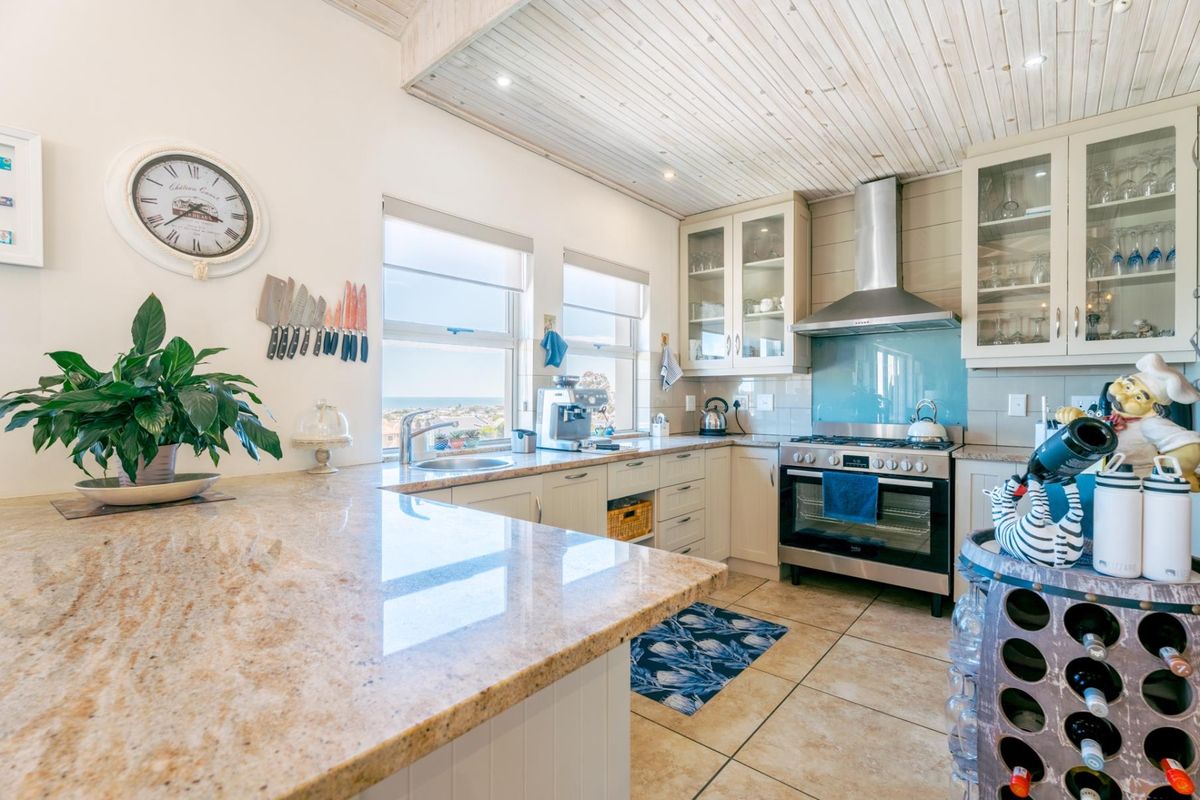 A well-appointed kitchen featuring granite countertops, glass-front cabinetry, a stainless steel gas stove, and a unique timber-clad ceiling with ocean views.