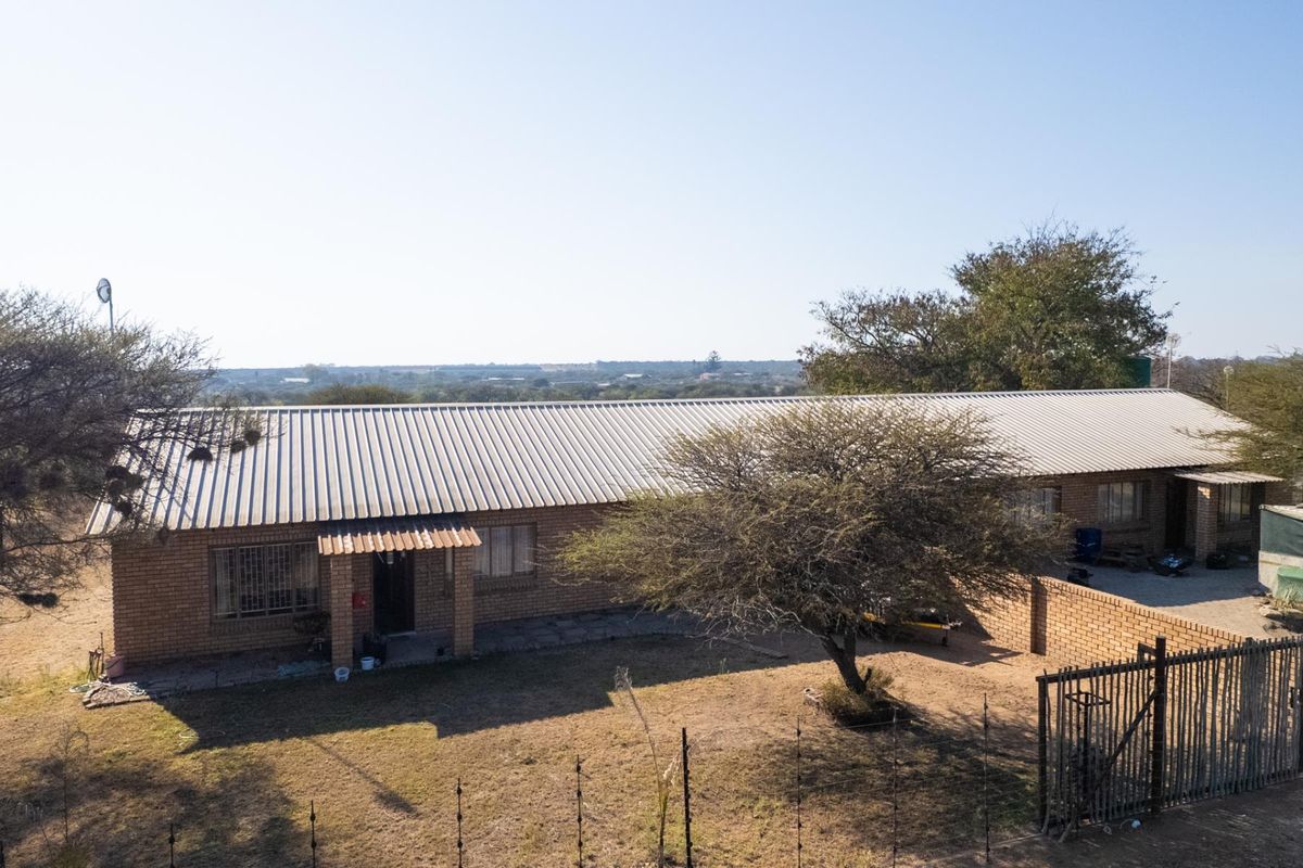Aerial view of a single-story face brick farmhouse with a corrugated metal roof, featuring a surrounding yard and boundary wall in a rural setting.