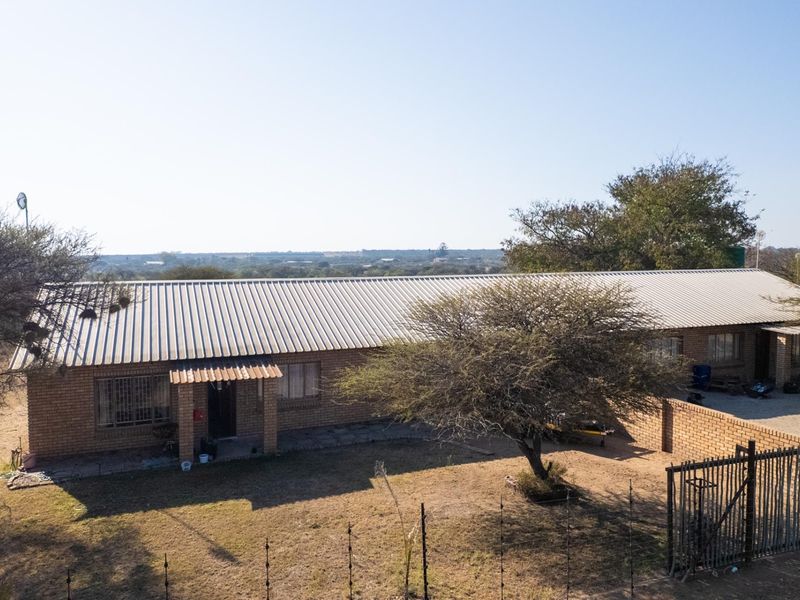 Aerial view of a single-story face brick farmhouse with a corrugated metal roof, featuring a surrounding yard and boundary wall in a rural setting.