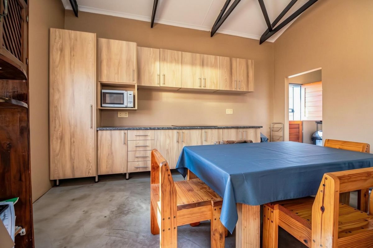 A functional kitchen featuring light wood-look cabinetry, laminate countertops, a built-in microwave, and exposed roof trusses, set against a neutral backdrop with concrete flooring.