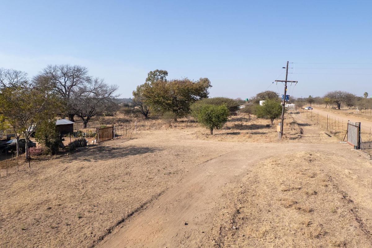 An aerial view of a rural farm property featuring a dirt driveway, perimeter wire fencing, and utility infrastructure set within a dry landscape.