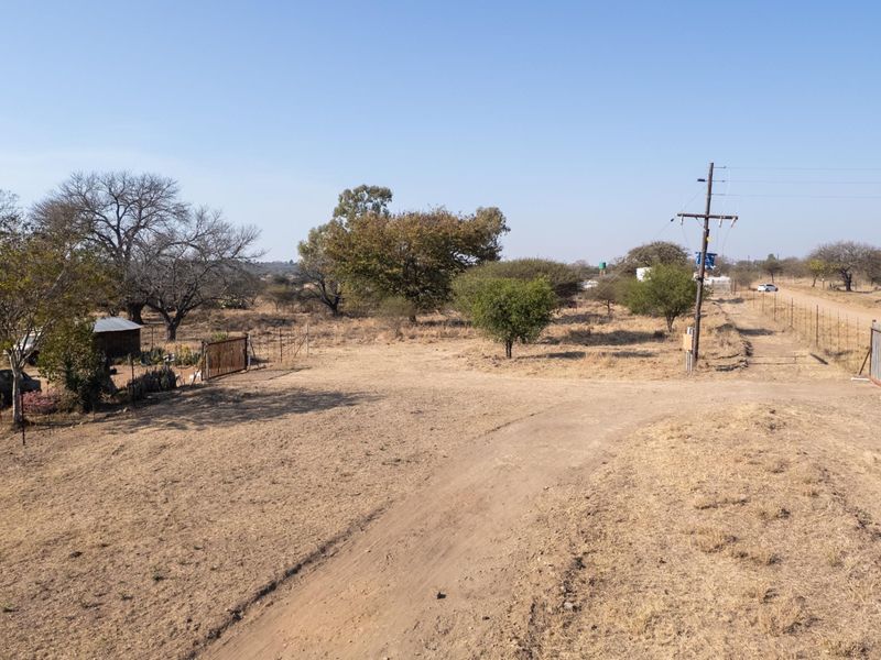 An aerial view of a rural farm property featuring a dirt driveway, perimeter wire fencing, and utility infrastructure set within a dry landscape.