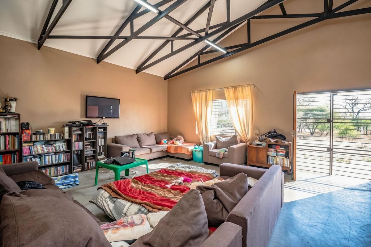 Spacious living area featuring high vaulted ceilings with exposed steel trusses, concrete flooring, and direct access to the exterior through a security gate.