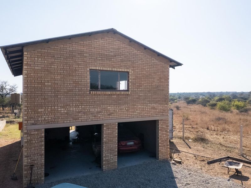 A two-story face brick building featuring a double garage on the ground level, situated on a rural farm property.