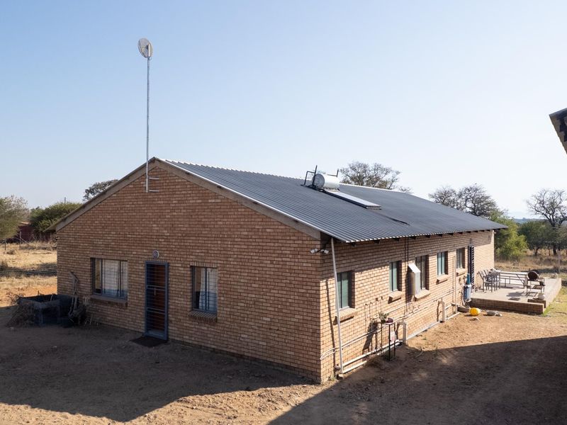 A rear view of a face brick farm dwelling featuring a corrugated metal roof, solar water heating system, and an attached concrete patio area.