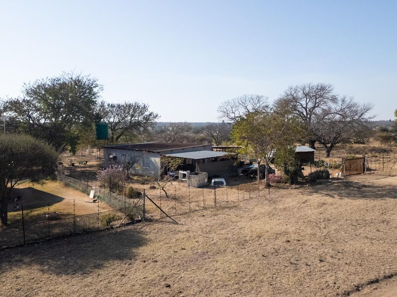 Aerial view of a rural farm property featuring a main dwelling, outbuildings, water storage tank, and surrounding fenced land.