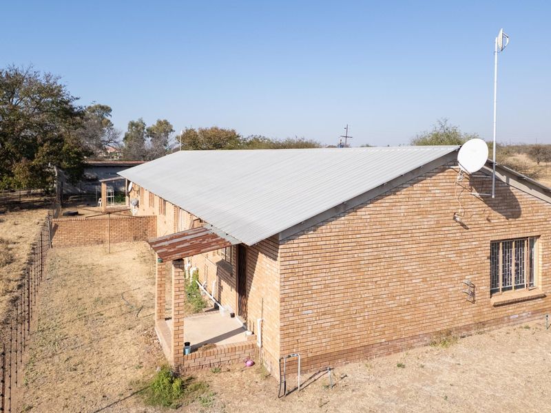 Aerial view of the rear elevation of a facebrick farmhouse featuring a corrugated metal roof, security bars on windows, and a small covered patio area.