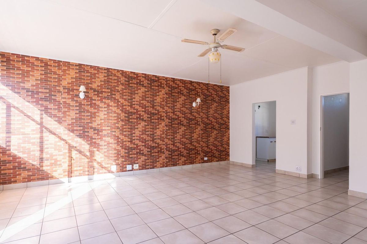 Spacious living area featuring a brick-style accent wall, neutral ceramic floor tiles, and a ceiling fan, offering a bright and versatile open-plan layout.
