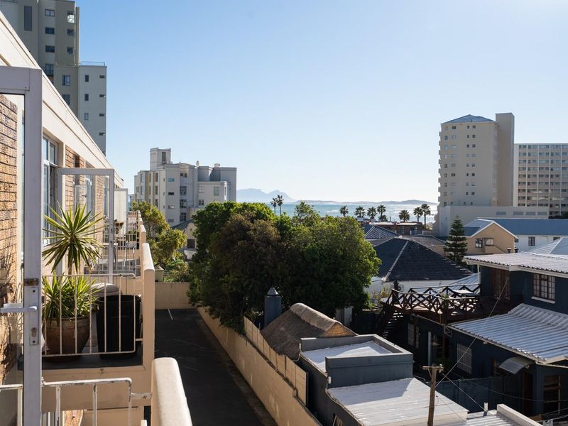 An elevated urban view overlooking surrounding apartment buildings and rooftops with a distant sea horizon.