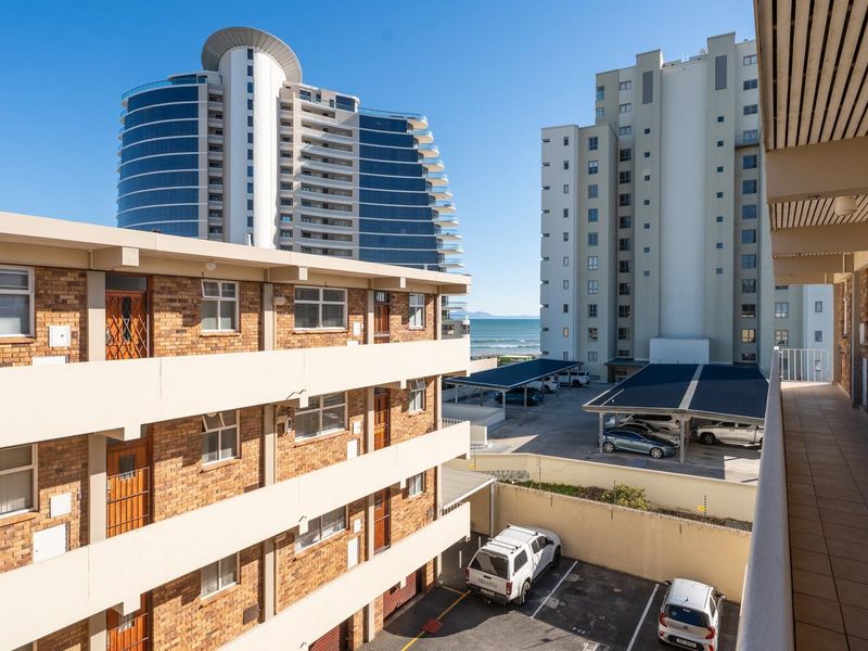 Elevated view overlooking the apartment complex exterior, parking area, and distant ocean horizon.