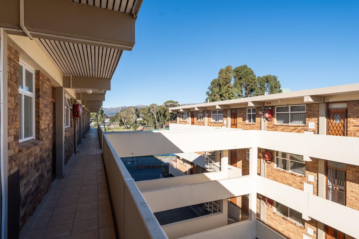 An exterior view of an apartment complex walkway featuring brick facade construction and open-air access to residential units.