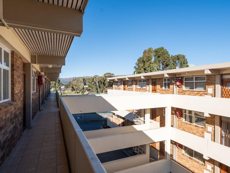 An exterior view of an apartment complex walkway featuring brick facade construction and open-air access to residential units.