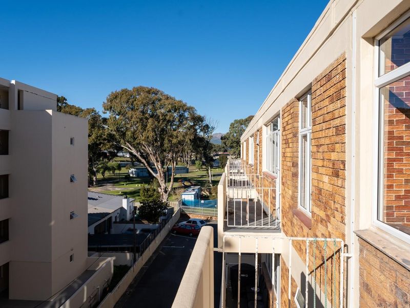 An elevated balcony view overlooking the apartment complex grounds and surrounding neighborhood, featuring brick exterior walls and metal safety railings.