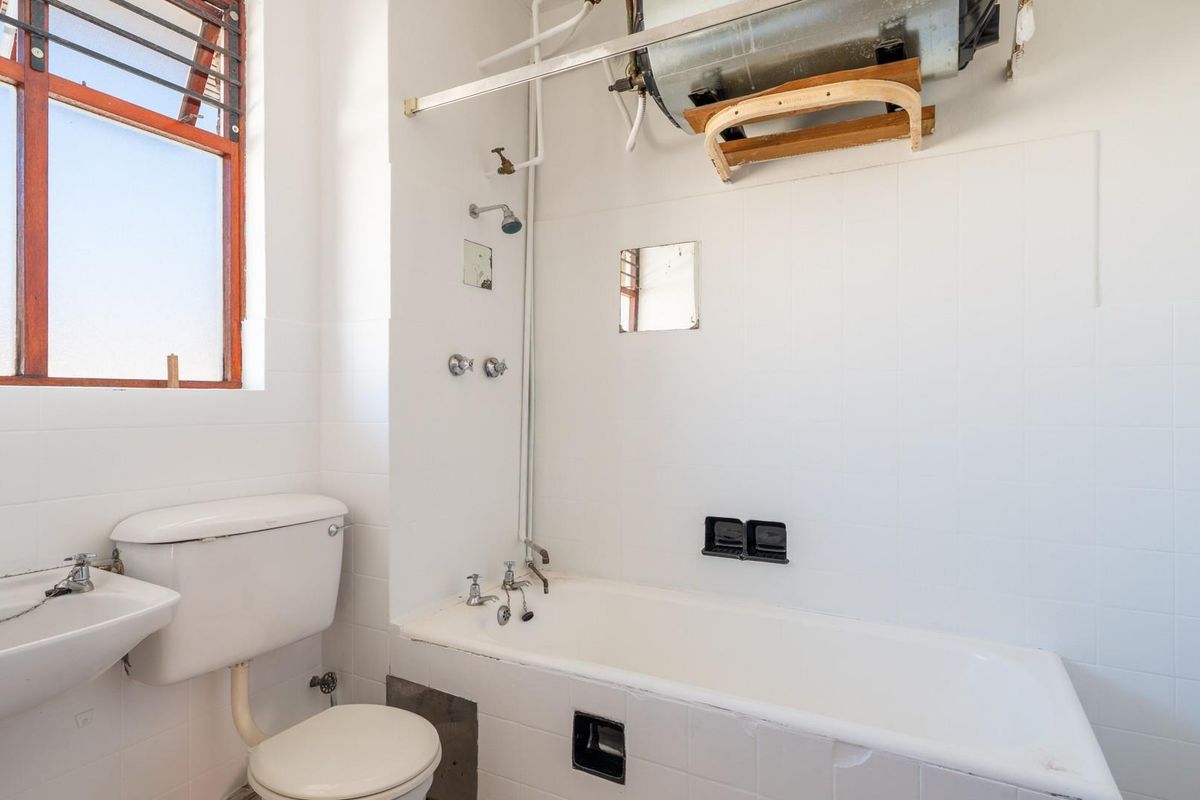 A functional bathroom featuring a bathtub with shower attachment, pedestal basin, and toilet, with exposed water heater and dated finishes.
