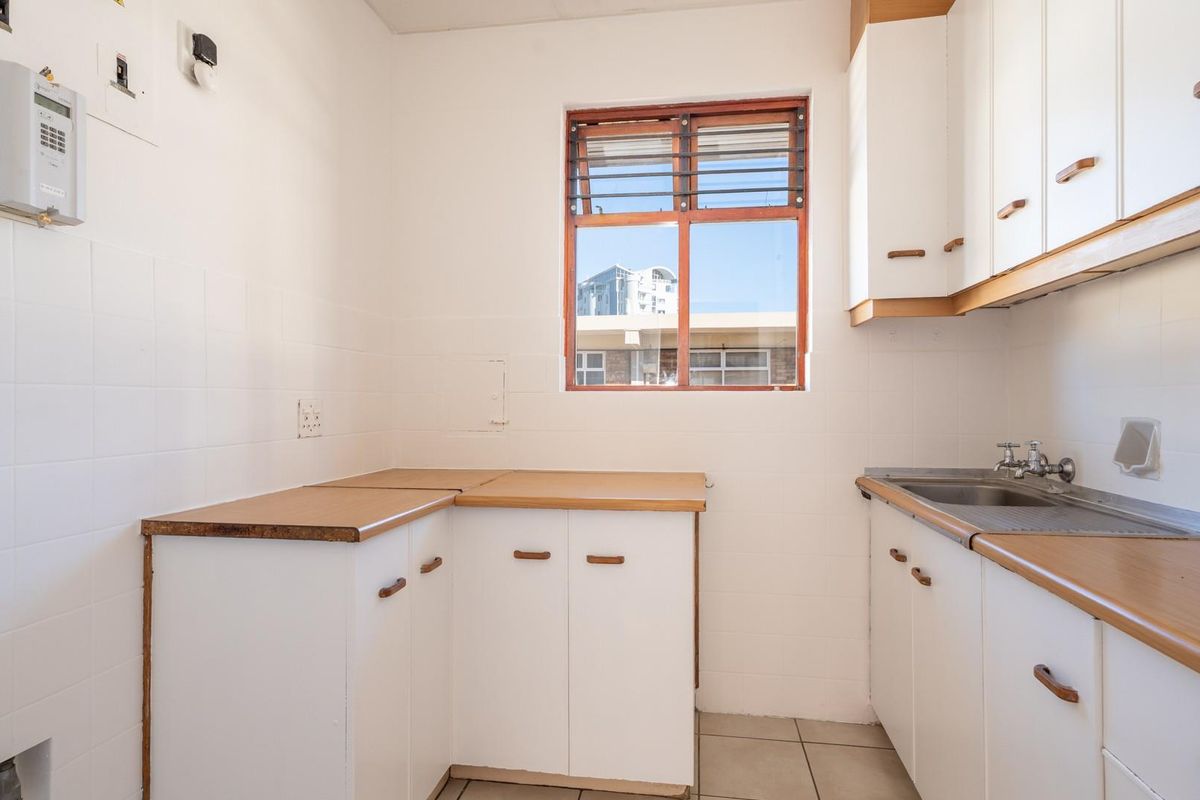 A functional, empty kitchen featuring white cabinetry, laminate countertops, a stainless steel sink, and tiled splashbacks, offering a blank canvas for renovation.