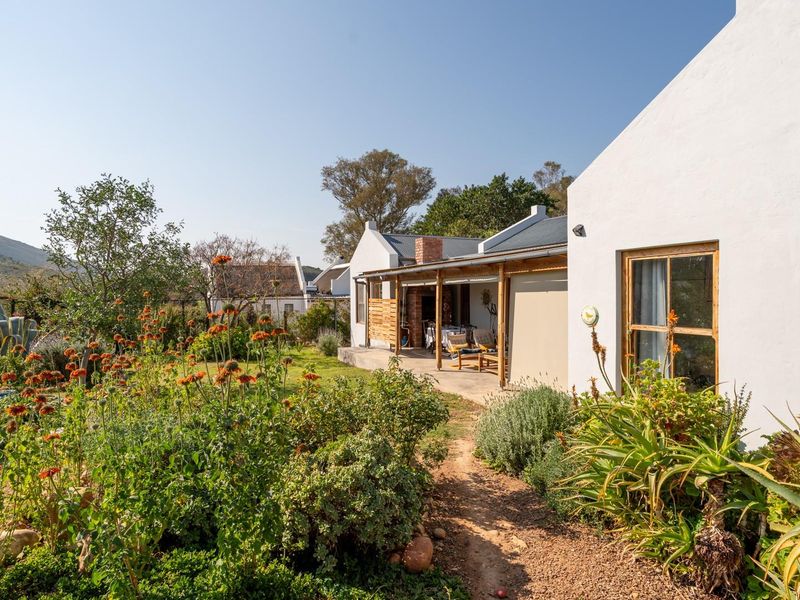 A view of the rear exterior featuring a covered patio, timber-framed windows, and a well-maintained garden with mountain views in the background.