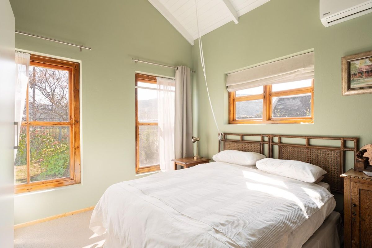 A bright bedroom featuring a vaulted ceiling, timber-framed windows, and a wall-mounted air conditioning unit.