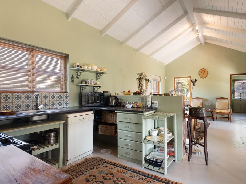Open-plan kitchen and living area featuring a vaulted ceiling with exposed beams, a wood-burning stove, and functional cabinetry with a tiled backsplash.