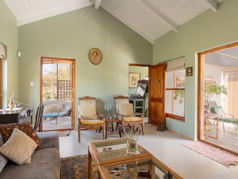 A bright living room featuring a vaulted ceiling with exposed beams, concrete flooring, and multiple access points to outdoor patio areas.