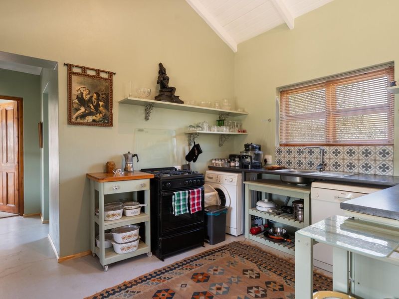 A functional kitchen featuring a gas stove, tiled backsplash, stainless steel sink, and open shelving under a vaulted ceiling.