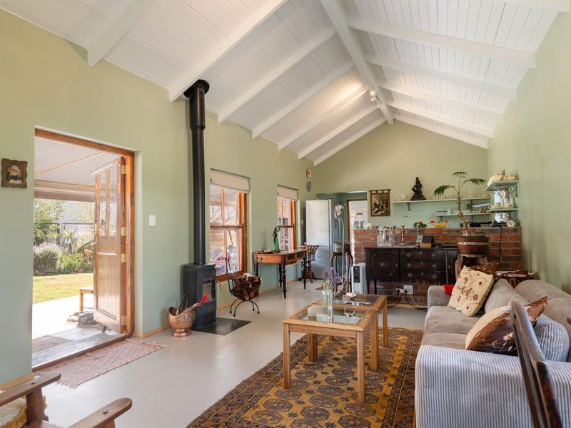 Spacious living room featuring a high vaulted timber ceiling, exposed beams, a freestanding wood-burning fireplace, and an exposed brick wall with direct garden access.