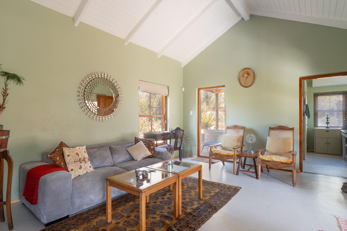 A spacious living room featuring a high vaulted ceiling with exposed beams, painted concrete floors, and direct access to an outdoor patio area.