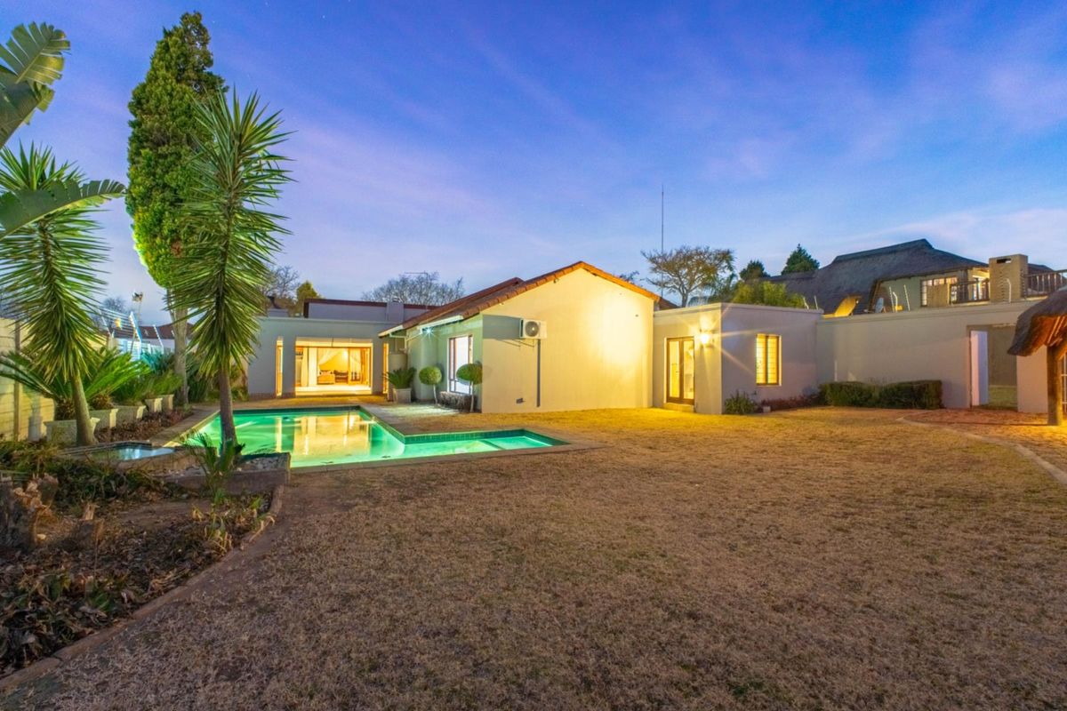 A well-maintained rear exterior view featuring a swimming pool, landscaped garden, and illuminated building facade at dusk.