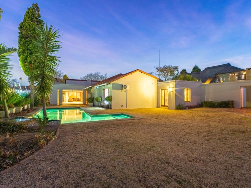 A well-maintained rear exterior view featuring a swimming pool, landscaped garden, and illuminated building facade at dusk.