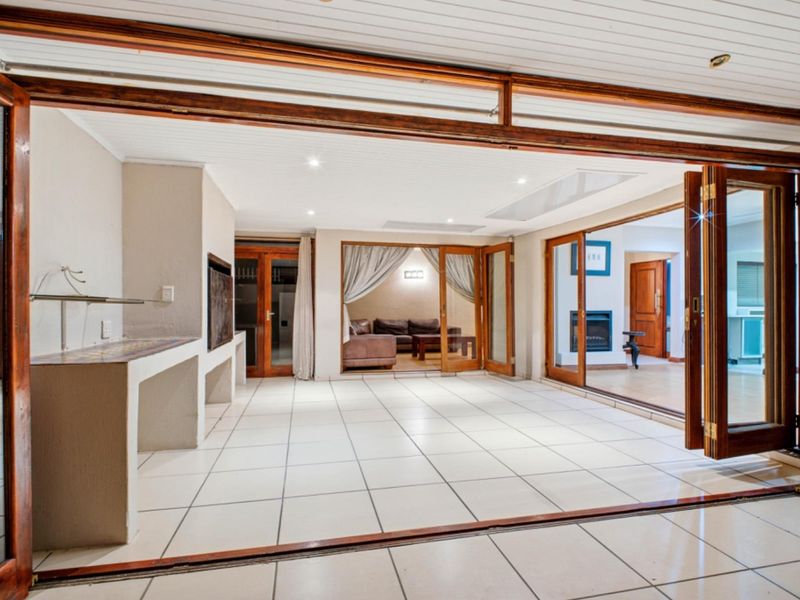 Spacious covered patio featuring tiled flooring, a built-in braai, and large timber-framed folding doors that open to the interior living areas.