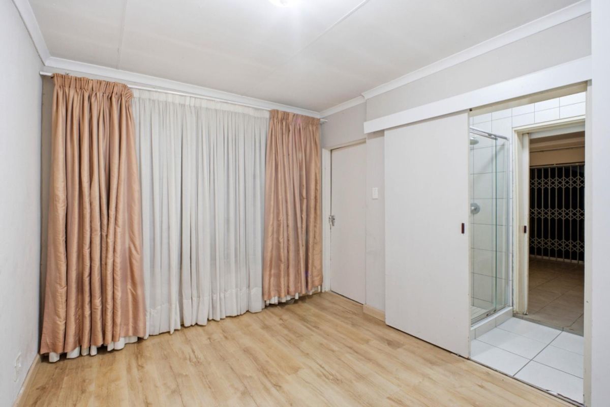 A clean, empty bedroom featuring laminate flooring, coving, and an integrated en-suite shower room with a sliding door entry.