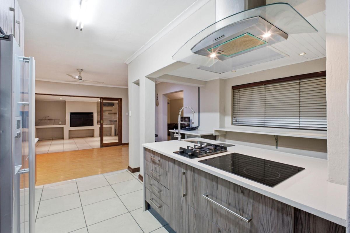 Modern kitchen featuring a dual gas and electric cooktop, glass extractor fan, stone countertops, and sleek cabinetry, flowing into an adjacent living area.